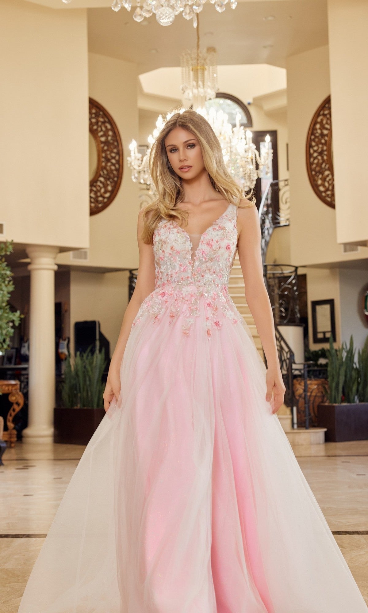 A woman in the Nox Anabel Y1799 long prom dress, featuring pastel tulle and delicate floral embellishments, stands in a grand foyer with chandeliers and ornate decor.